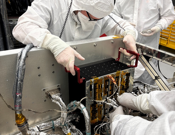 In the clean room at the Johns Hopkins Applied Physics Laboratory in Laurel, Maryland, Emory Toomey (left) and Hunter Reeling integrate the engineering model of Dragonfly’s Integrated Electronics Module (IEM), which contains the spacecraft’s core avionics, with the lander’s electrical harness, which is the bundled assembly of wires, cables, and connectors that will transmit power and data throughout the rotorcraft. Credit: NASA/Johns Hopkins APL